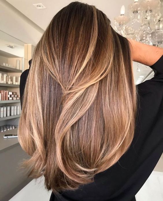 Cabelo longo e liso com mechas loiras, visto de costas, em ambiente de salão de beleza.