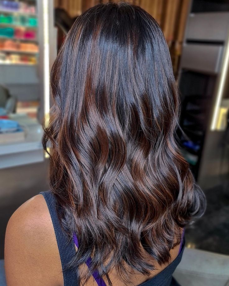 mechas-impecaveis Pessoa de costas com cabelo castanho ondulado em ambiente interno.