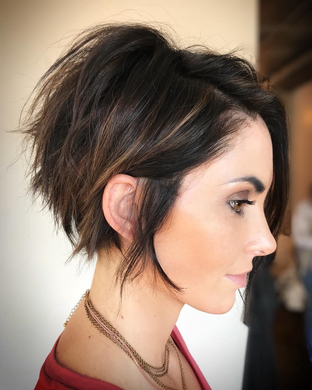 Pessoa de perfil com cabelo curto e escuro, usando colar de correntes, em ambiente interno.