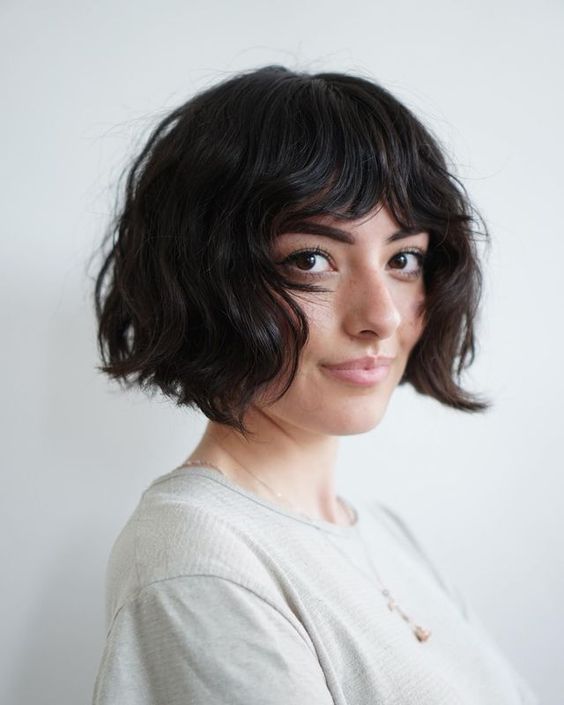 Pessoa com cabelo curto e ondulado, usando camiseta clara, olhando para a câmera, com fundo branco.