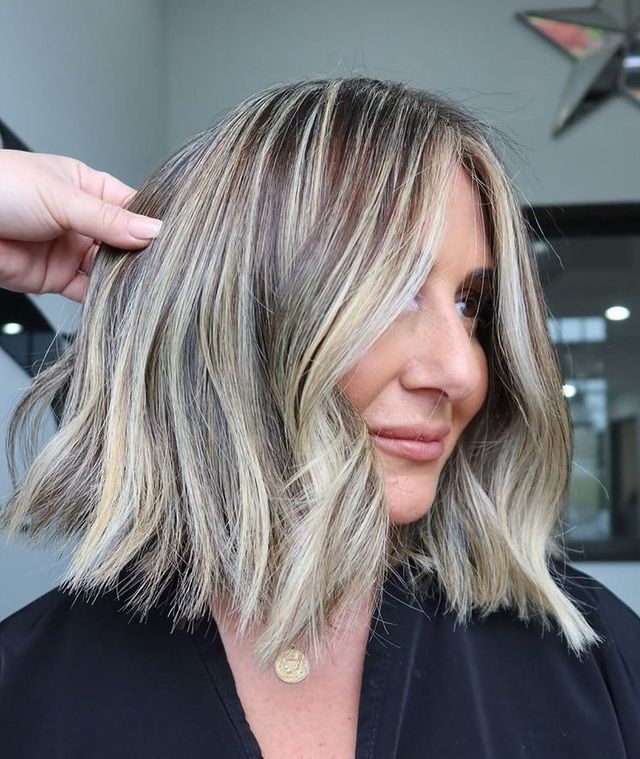 Mulher com cabelo loiro e castanho em corte médio, sendo estilizado por uma pessoa, em ambiente interno.