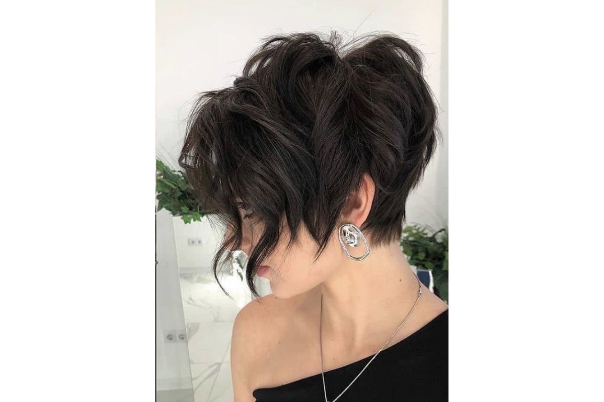 Cabelo curto e escuro em estilo pixie, com mechas onduladas na frente e brinco prateado grande.