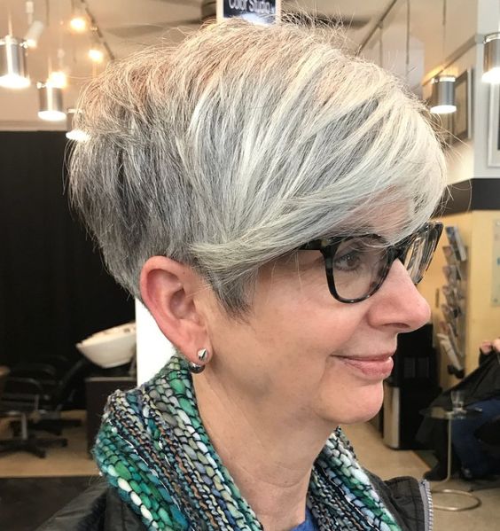 pixie-com-franja-lateral-apos-50-anos-pinterest Pessoa com cabelo curto grisalho e óculos, em perfil, dentro de um salão de beleza.