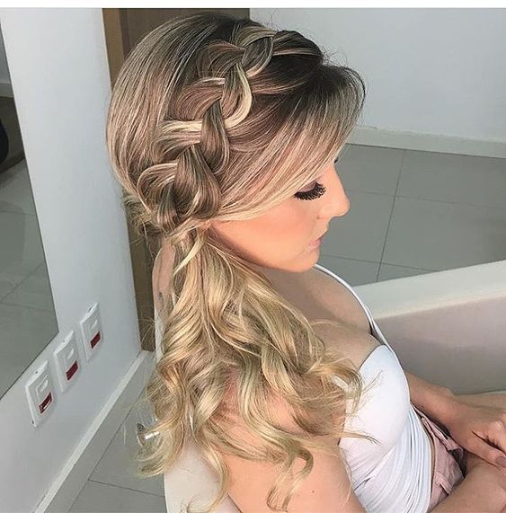Mulher com cabelo loiro trançado em estilo lateral, sentada em um ambiente interno.