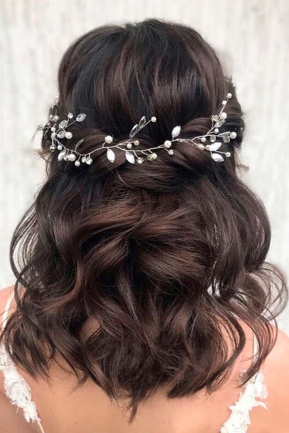 Cabelo castanho ondulado com tiara de flores e pérolas, visto de costas.