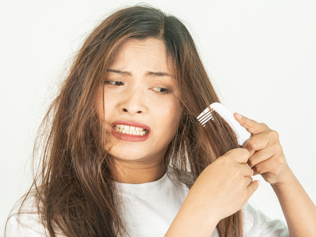 metodos-recuperar-cabelo-elastico Pessoa tentando desembaraçar cabelo com pente, expressão de esforço.